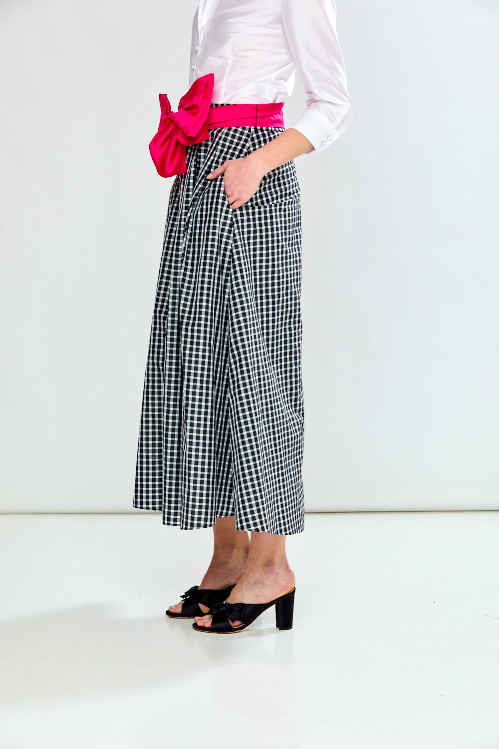 Person wearing a white blouse, black and white checkered skirt, pink belt, and black shoes on a white background