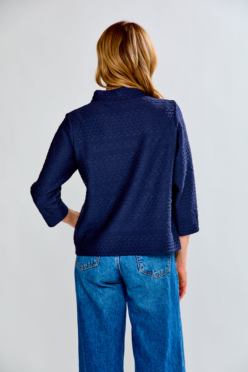 Woman wearing a navy blue textured sweater and blue jeans on a white background
