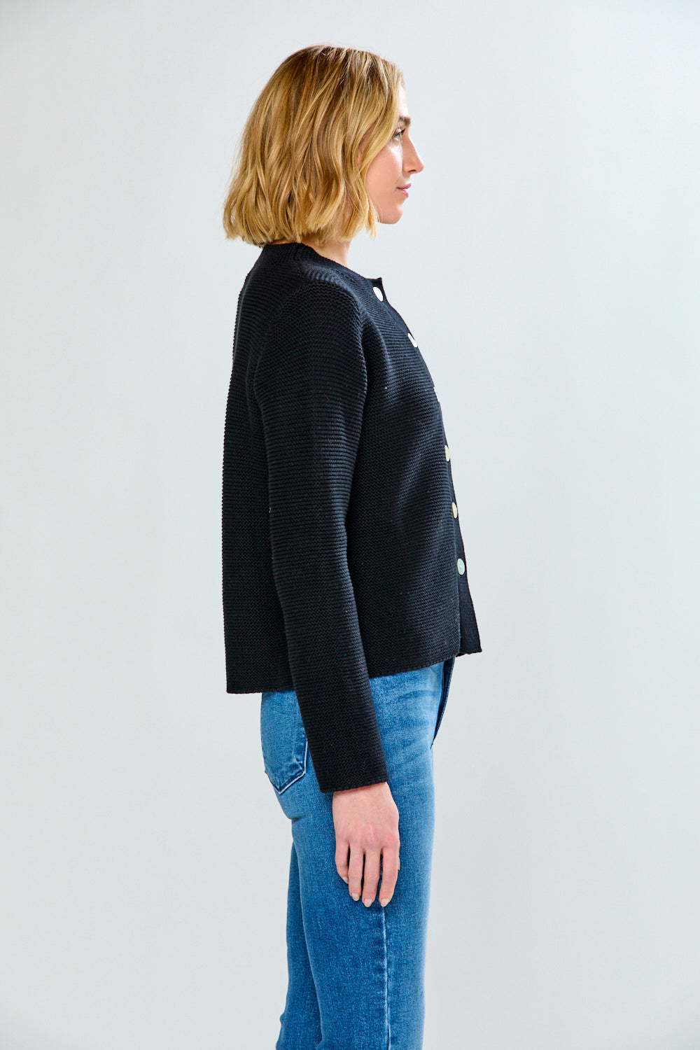 Side profile image of a woman wearing a black cardigan and jeans against a light grey background.
