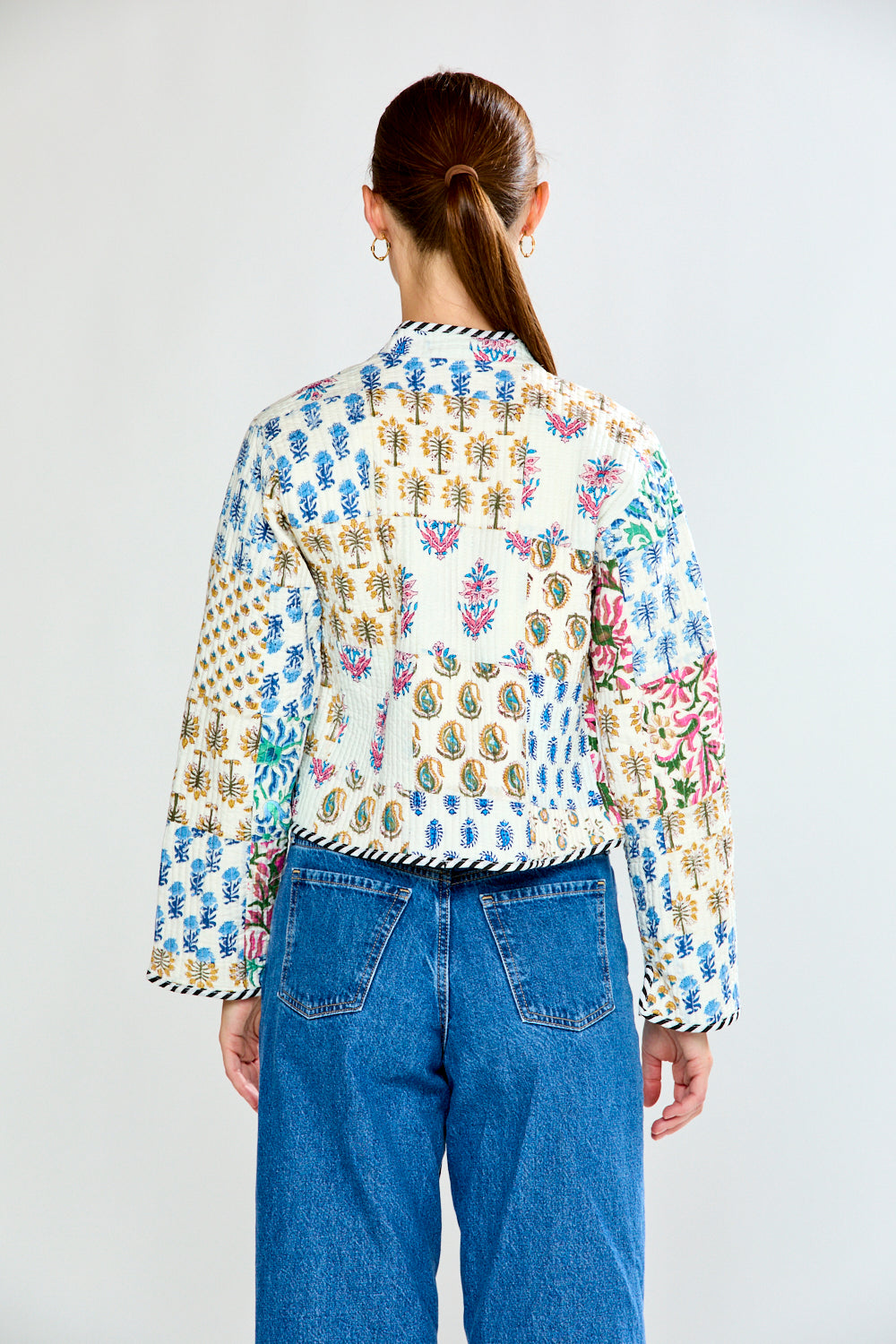 Person wearing a colorful patterned shirt and blue jeans on a white background