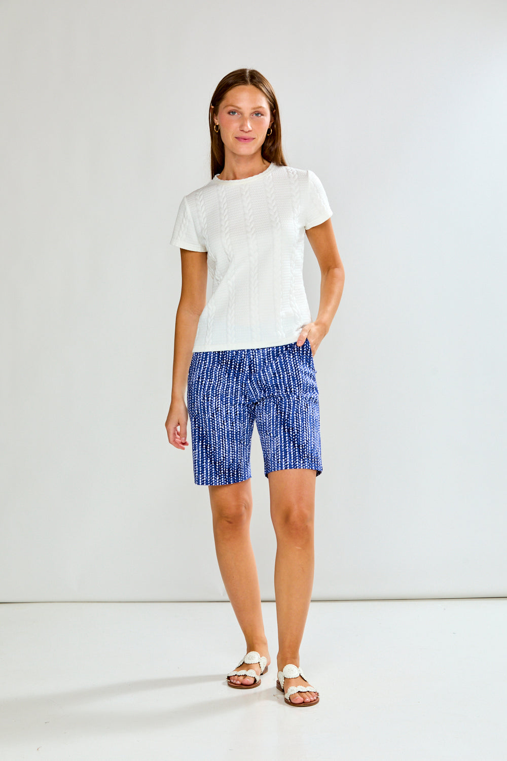Woman wearing a white t-shirt and blue shorts against a plain background