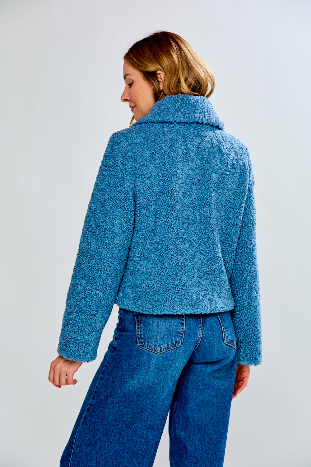 Person wearing a blue textured jacket and jeans on a light gray background