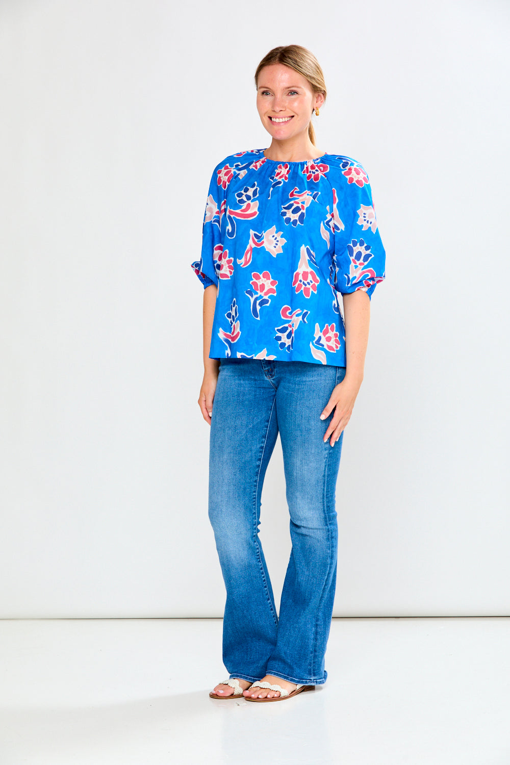 Woman wearing a blue floral blouse and jeans on a white background