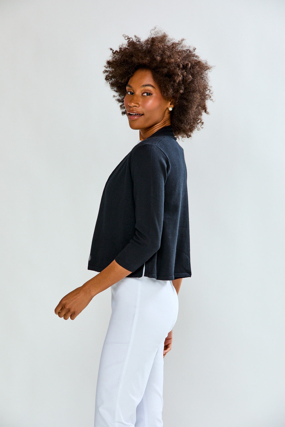 Woman wearing a dark blue sweater and white pants against a light gray background