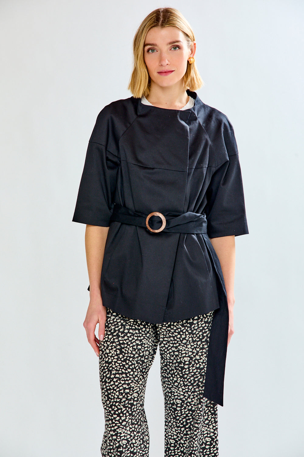Woman wearing a black belted jacket and patterned pants on a white background