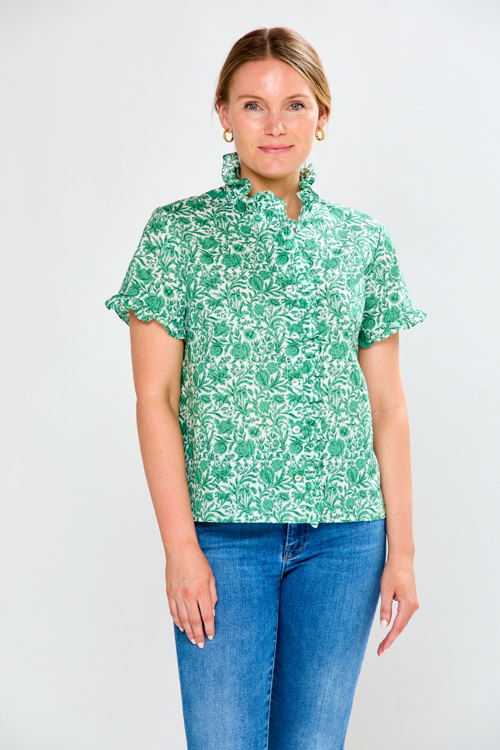 Woman wearing a green floral blouse and blue jeans on a white background