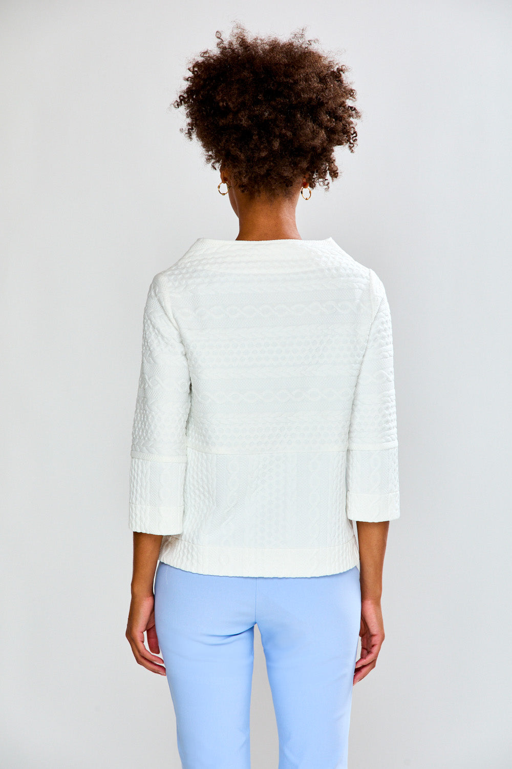 Person wearing a light-colored sweater and light blue pants on a plain background