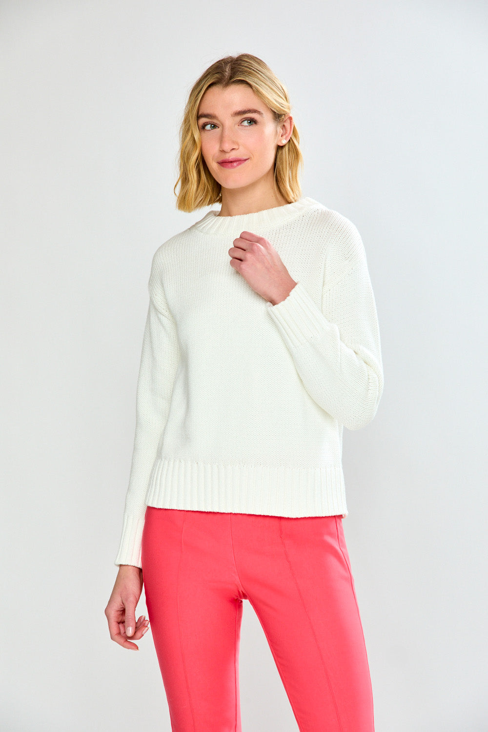 Woman wearing a white sweater and pink pants on a light gray background