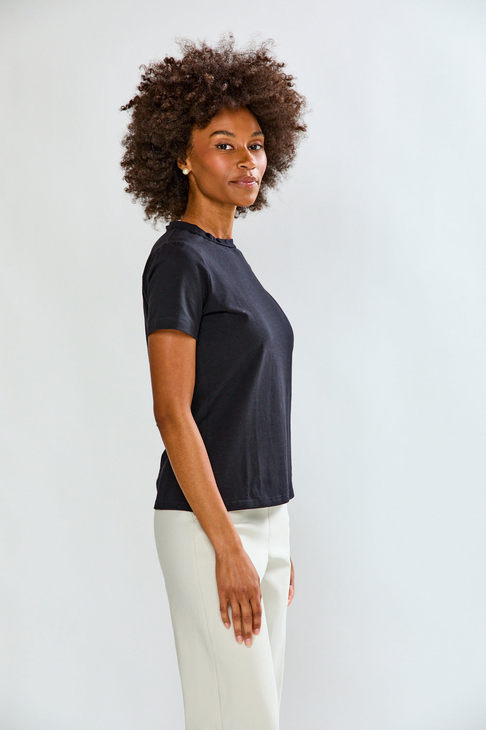 Woman wearing a black t-shirt and white pants against a plain background