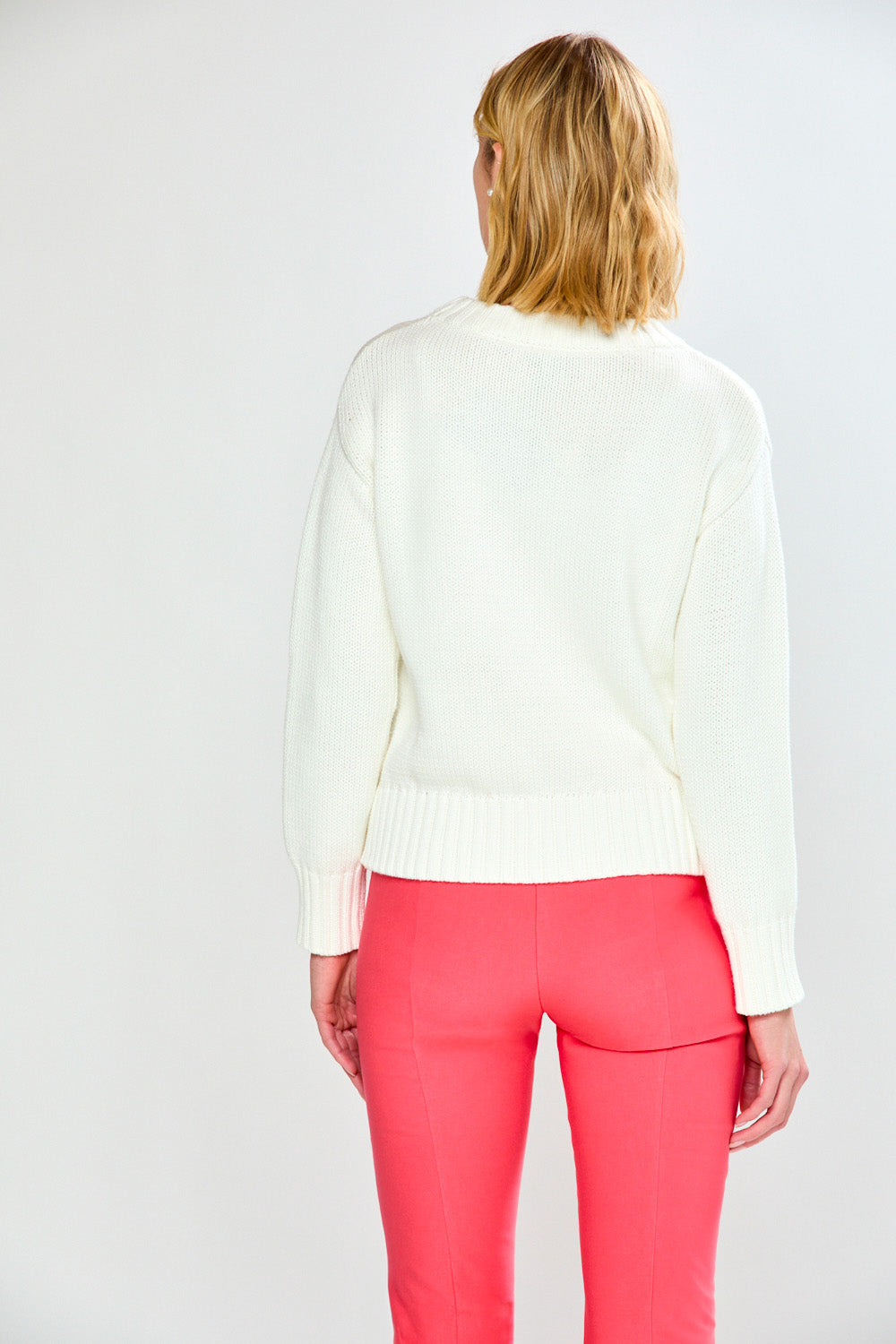 Woman wearing a white sweater and pink pants on a plain background
