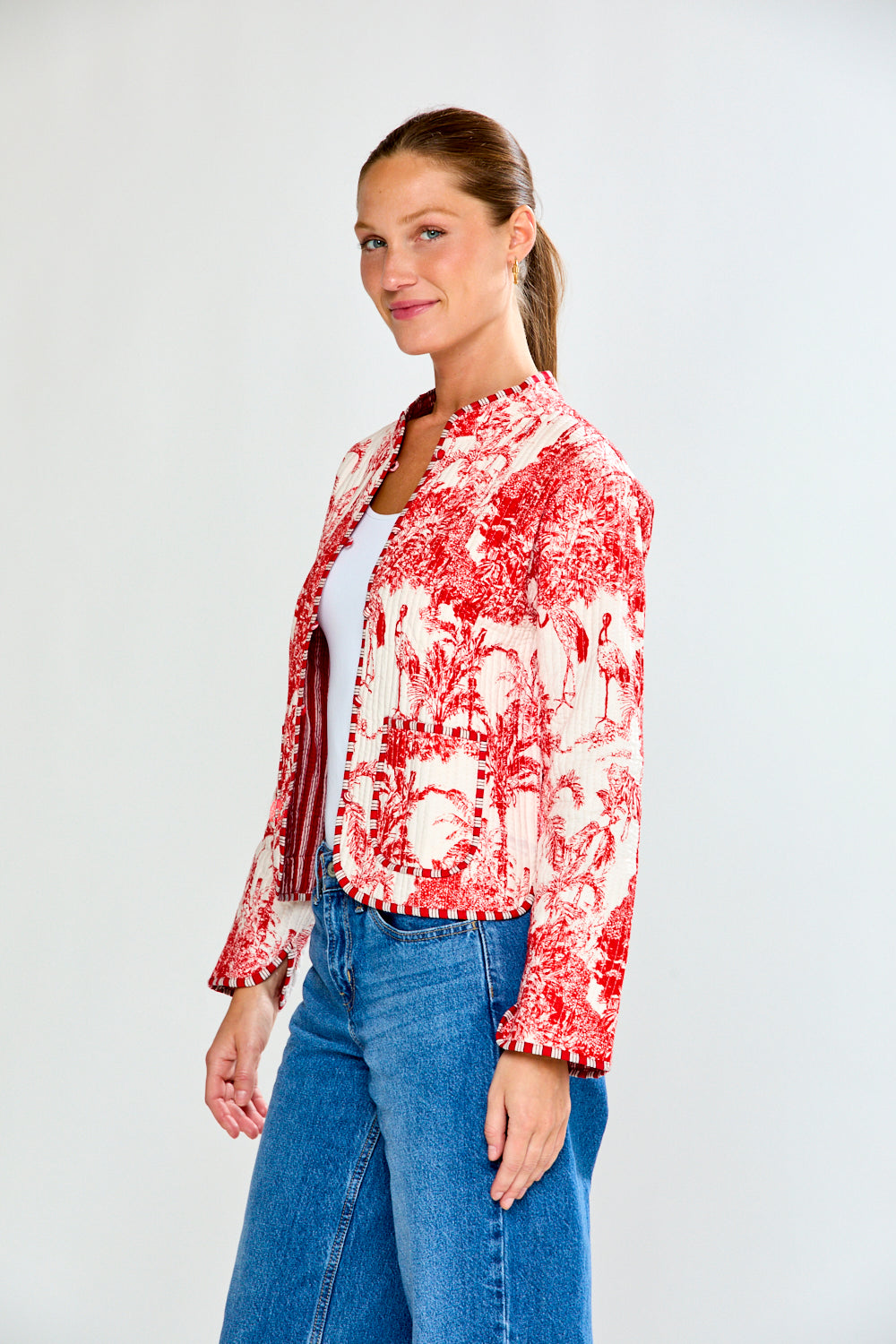 Woman wearing a red and white floral jacket with blue jeans on a white background