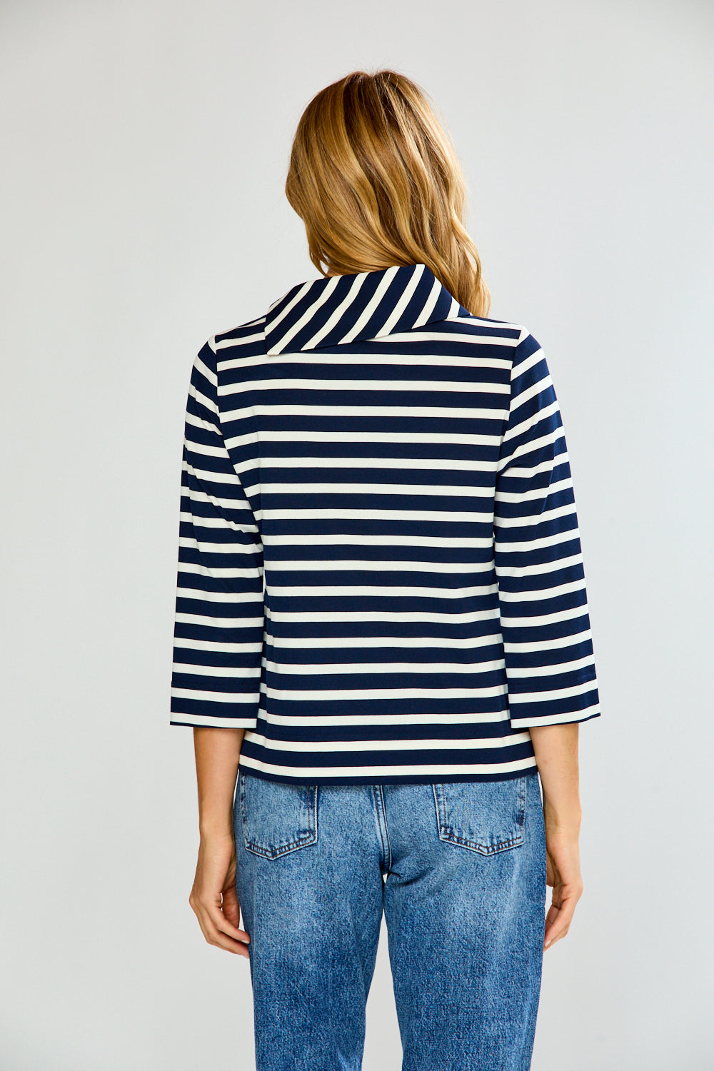 Person wearing a navy and white striped shirt with blue jeans on a plain background