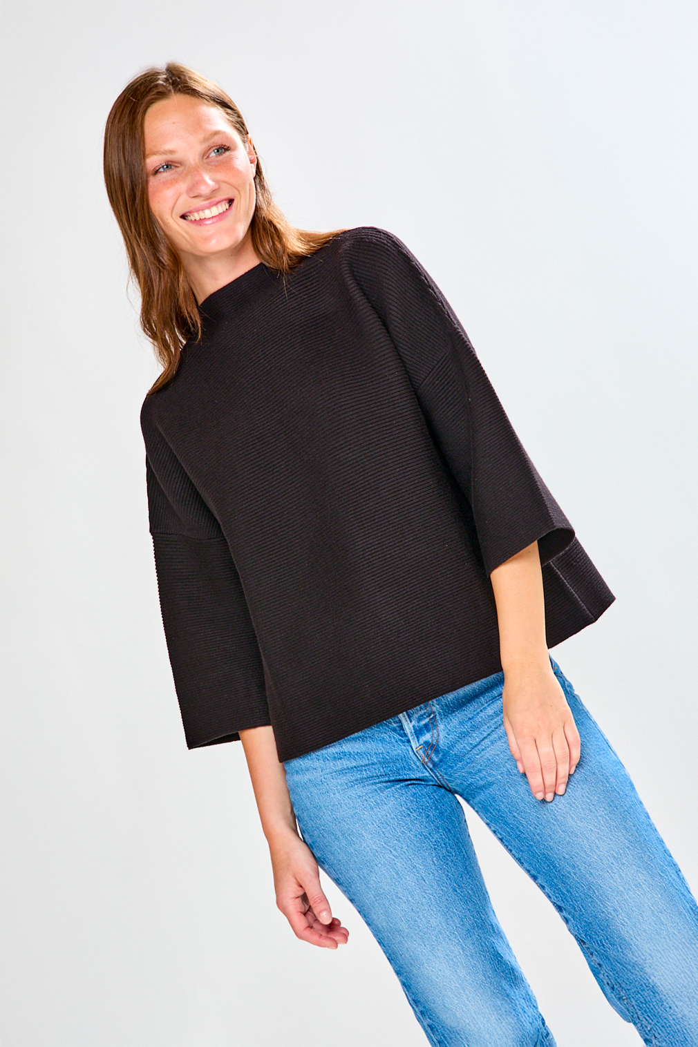 Woman wearing a black top and blue jeans on a white background