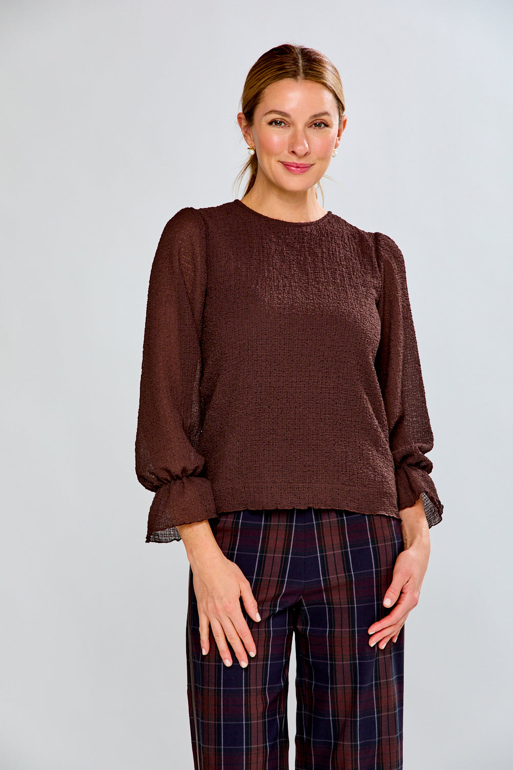 Woman wearing a brown blouse and plaid pants against a light gray background