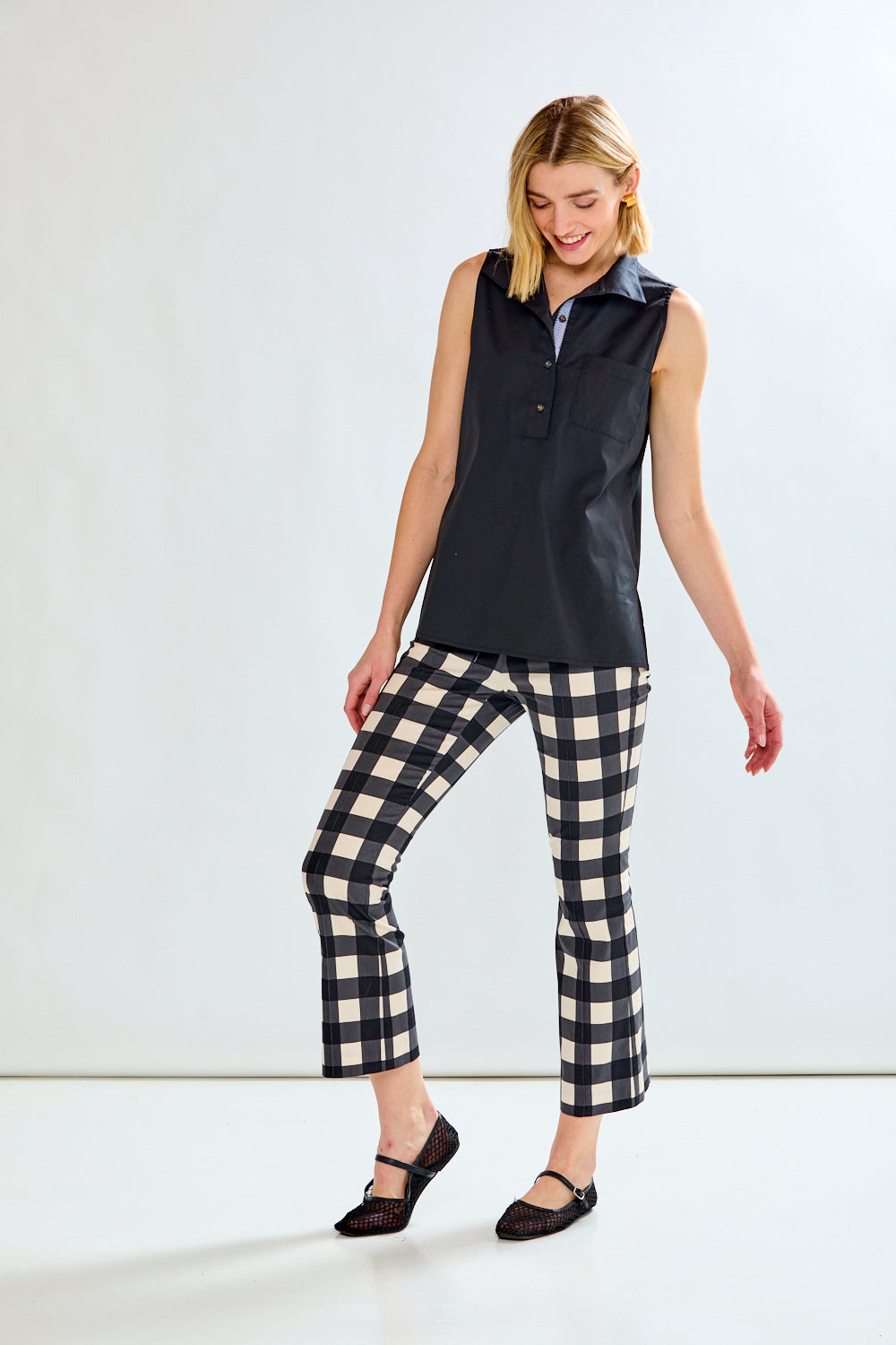 A woman modeling a sleeveless black collared top and black-and-white gingham cropped pants against a plain white studio background.