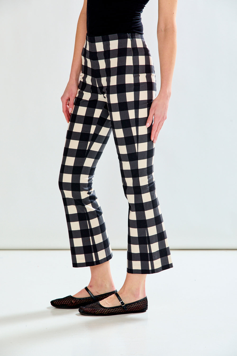 A model wearing black and cream buffalo check cropped flare pants with a black top and black flat shoes, shown from the waist down against a white studio background.