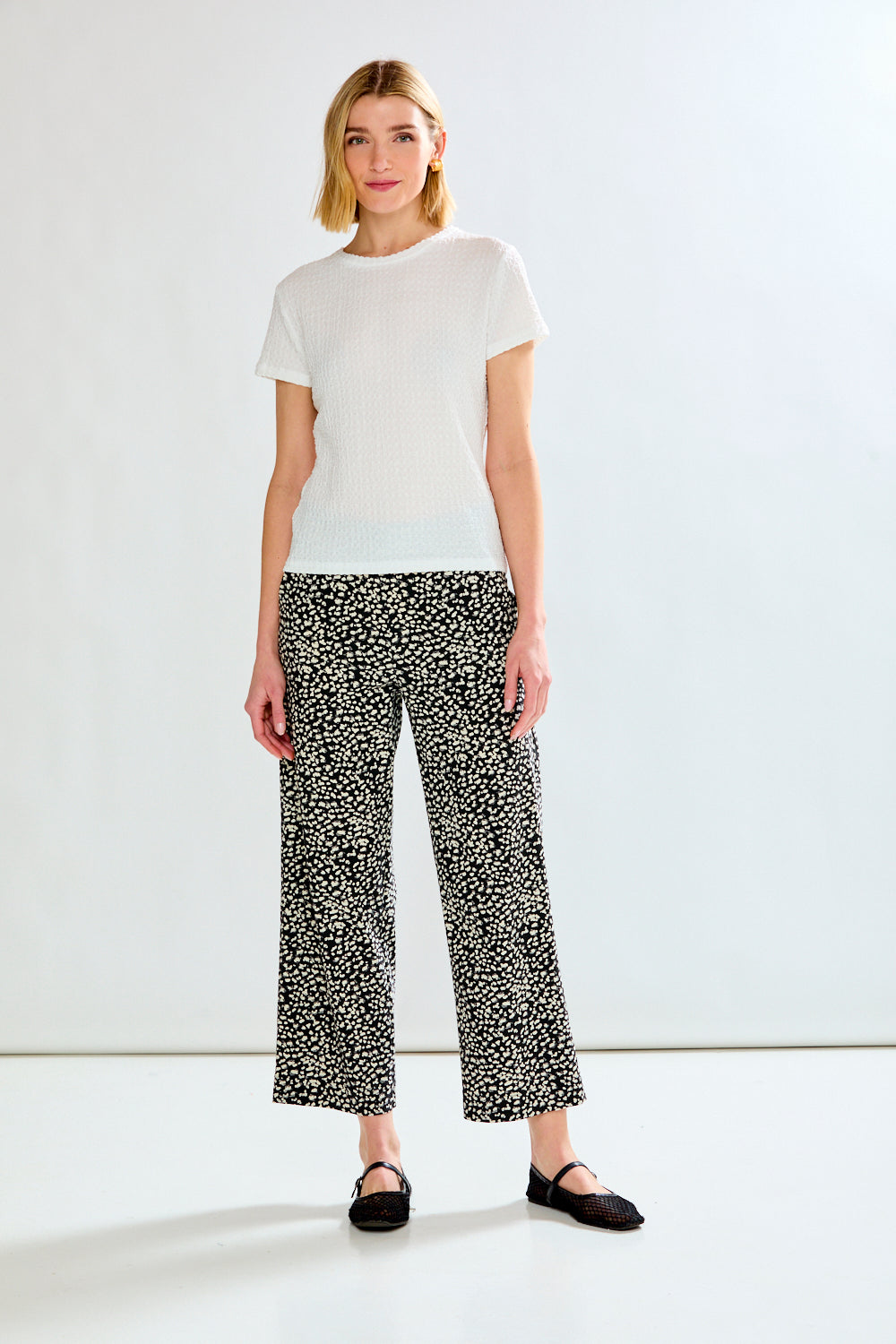 A woman modeling a white short-sleeve crewneck t-shirt and black-and-white patterned wide-leg cropped pants, paired with black flat shoes, against a clean white studio background.