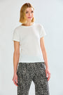 A woman modeling a short-sleeve white textured knit top paired with black and white patterned pants, shot against a light gray studio background.