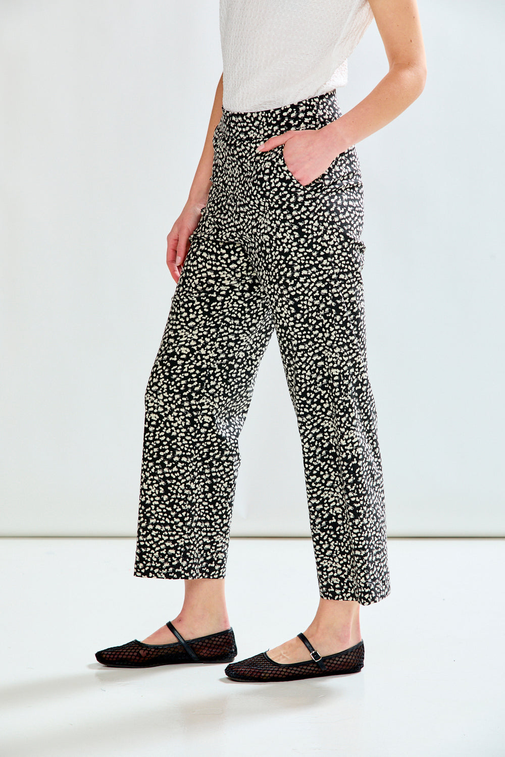 A model wearing black and white patterned cropped trousers, a white top, and black flat shoes, shown from the waist down against a plain white studio background.