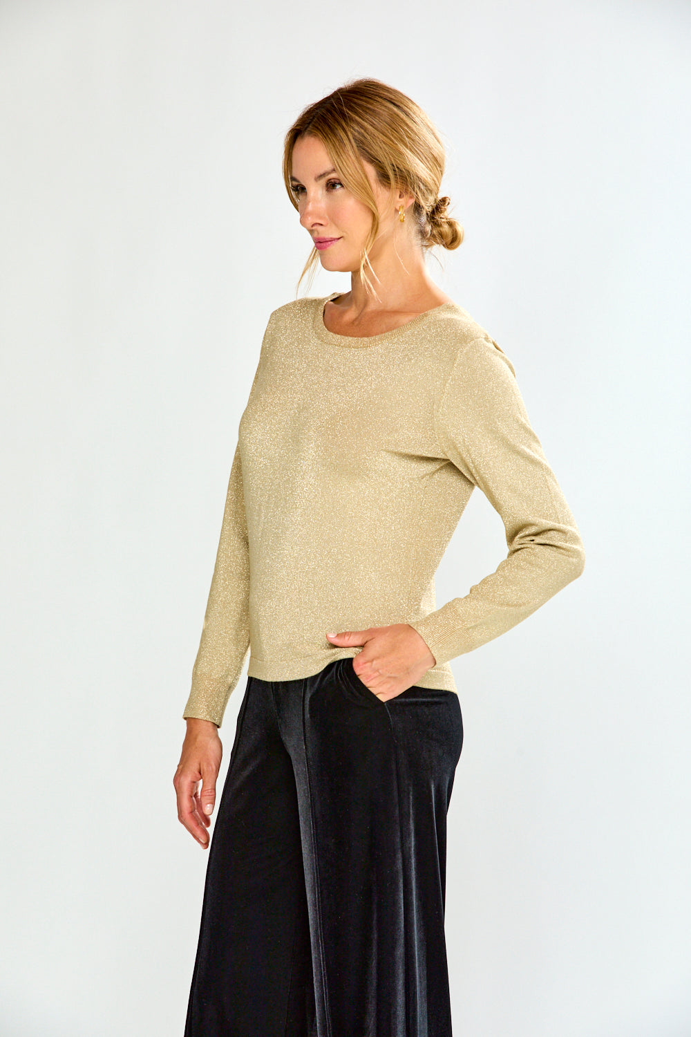 Woman wearing a gold sweater and black pants on a white background
