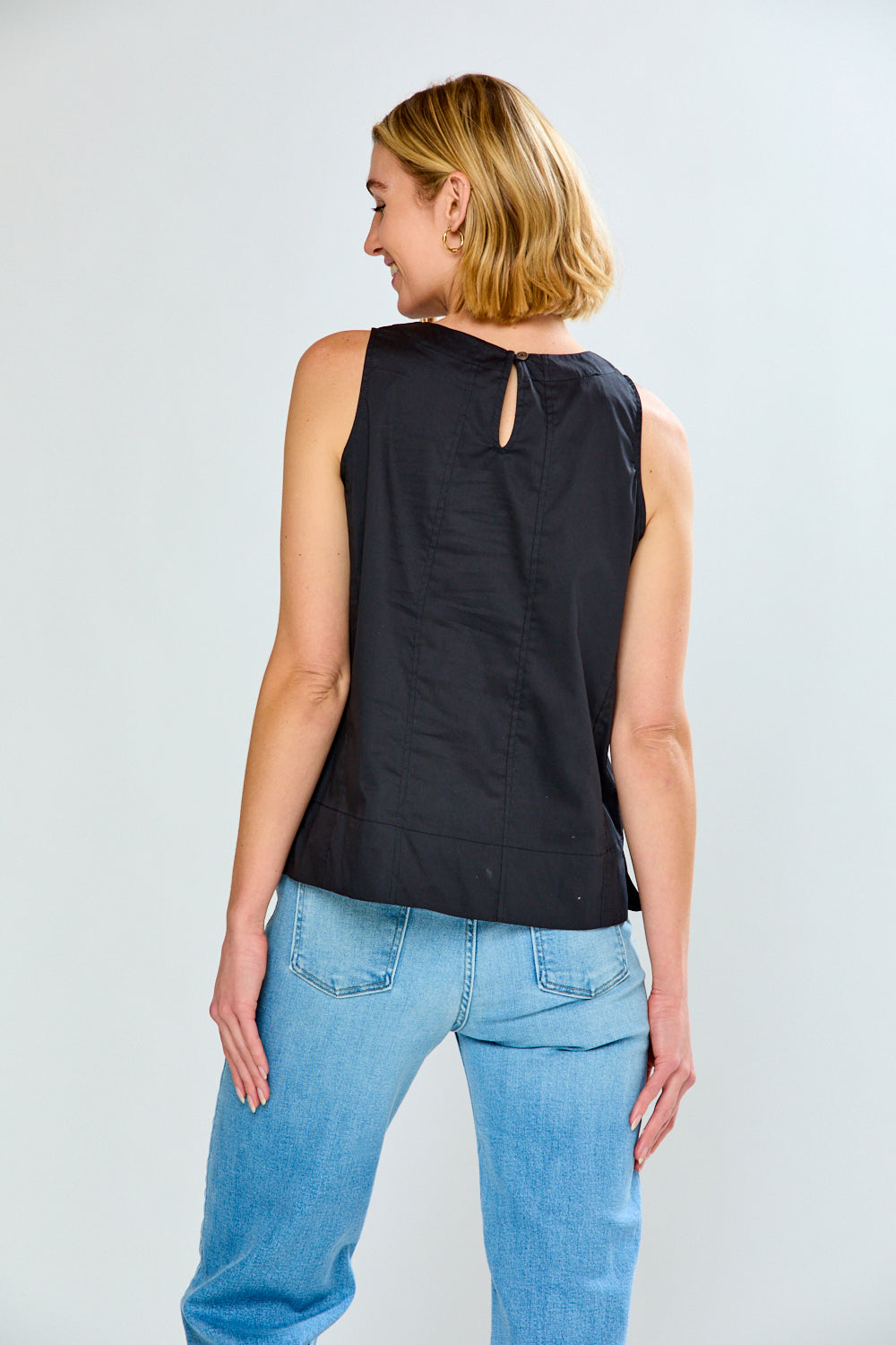 Woman wearing a black sleeveless top and blue jeans on a plain background