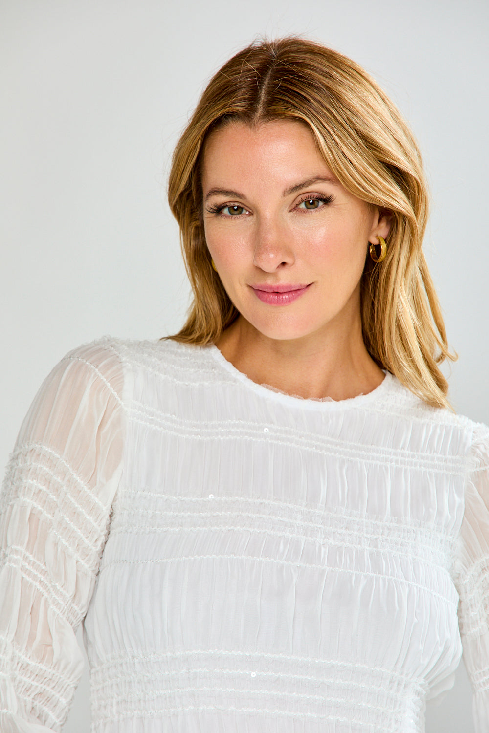 Woman wearing a white blouse with sheer sleeves against a plain background