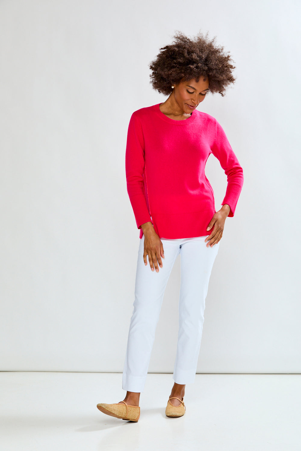 Woman wearing a bright pink sweater and white pants against a white background