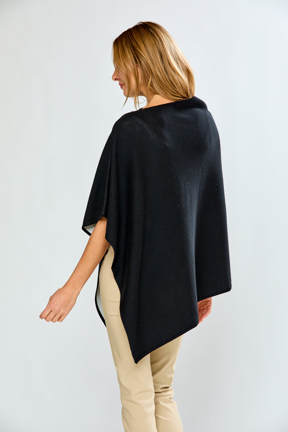 Woman wearing a black poncho over beige pants on a white background
