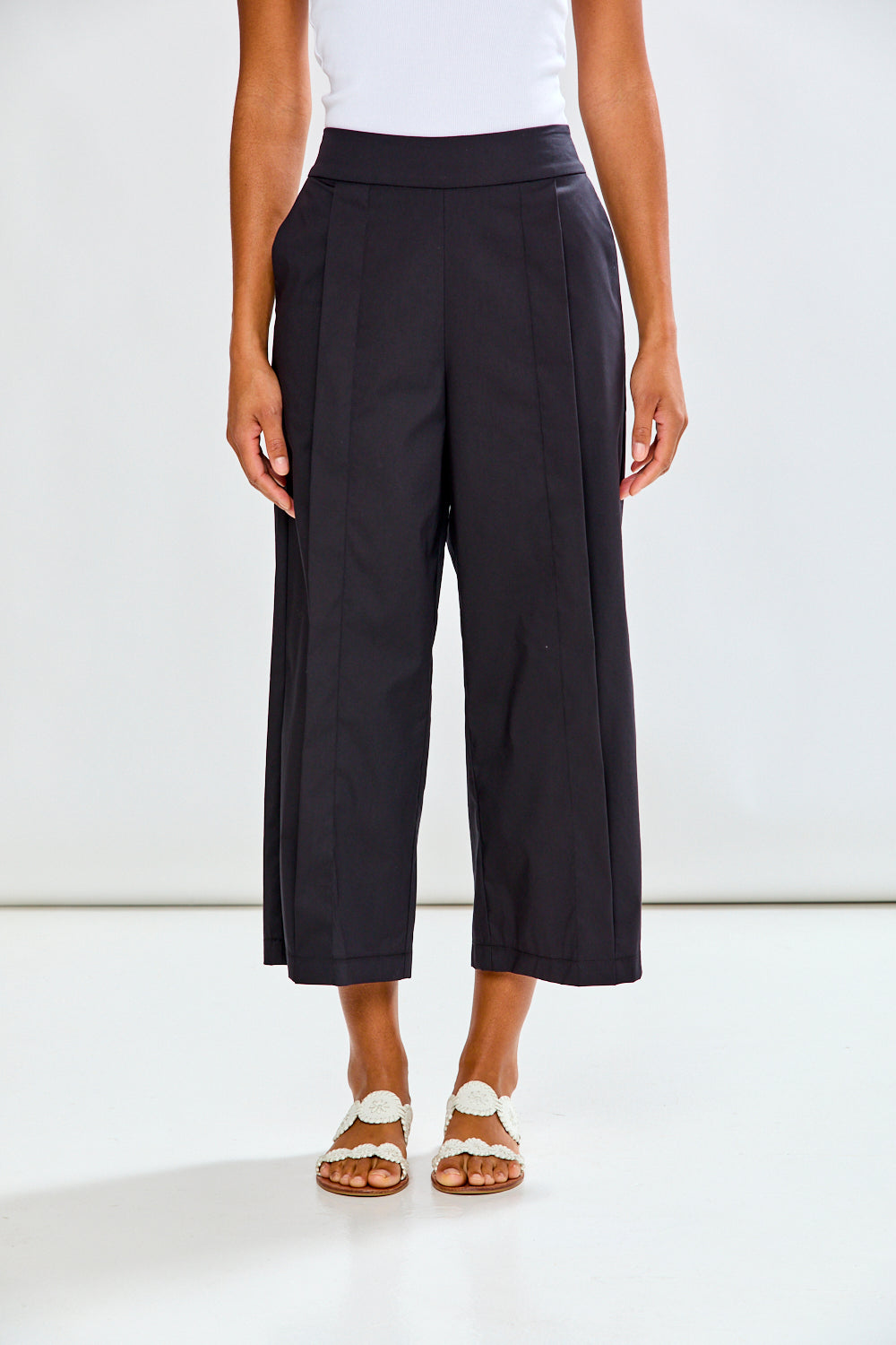 Woman wearing black wide-leg pants and white sandals on a white background