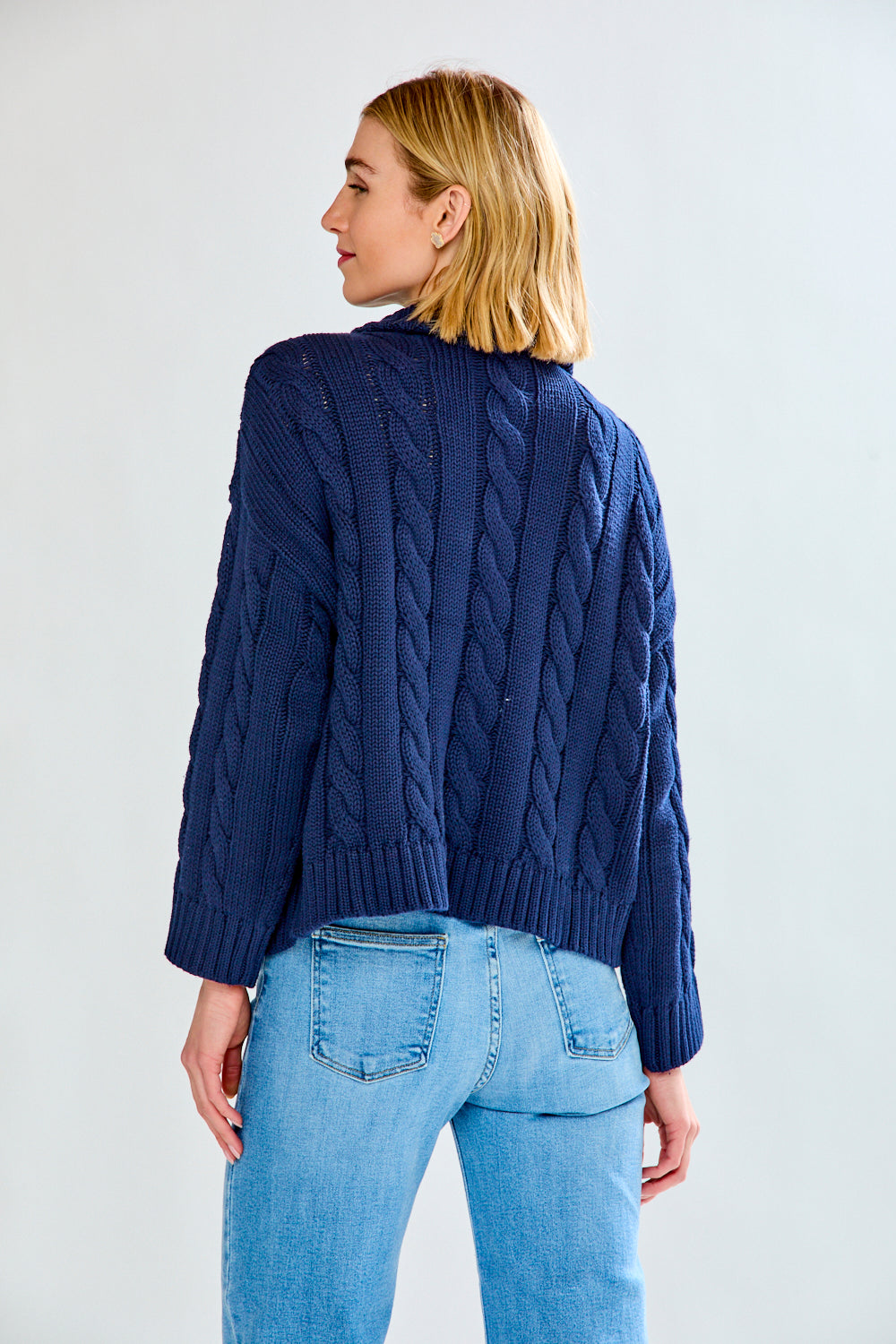 Woman wearing a navy cable knit sweater and blue jeans on a white background