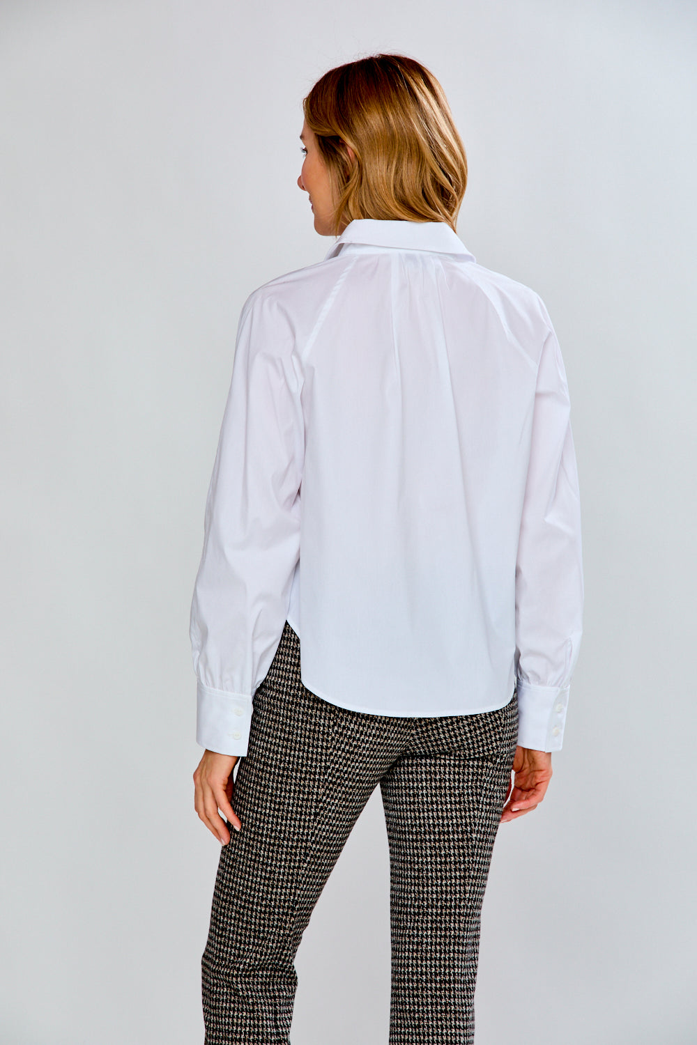 Woman wearing a white blouse and patterned pants against a plain background