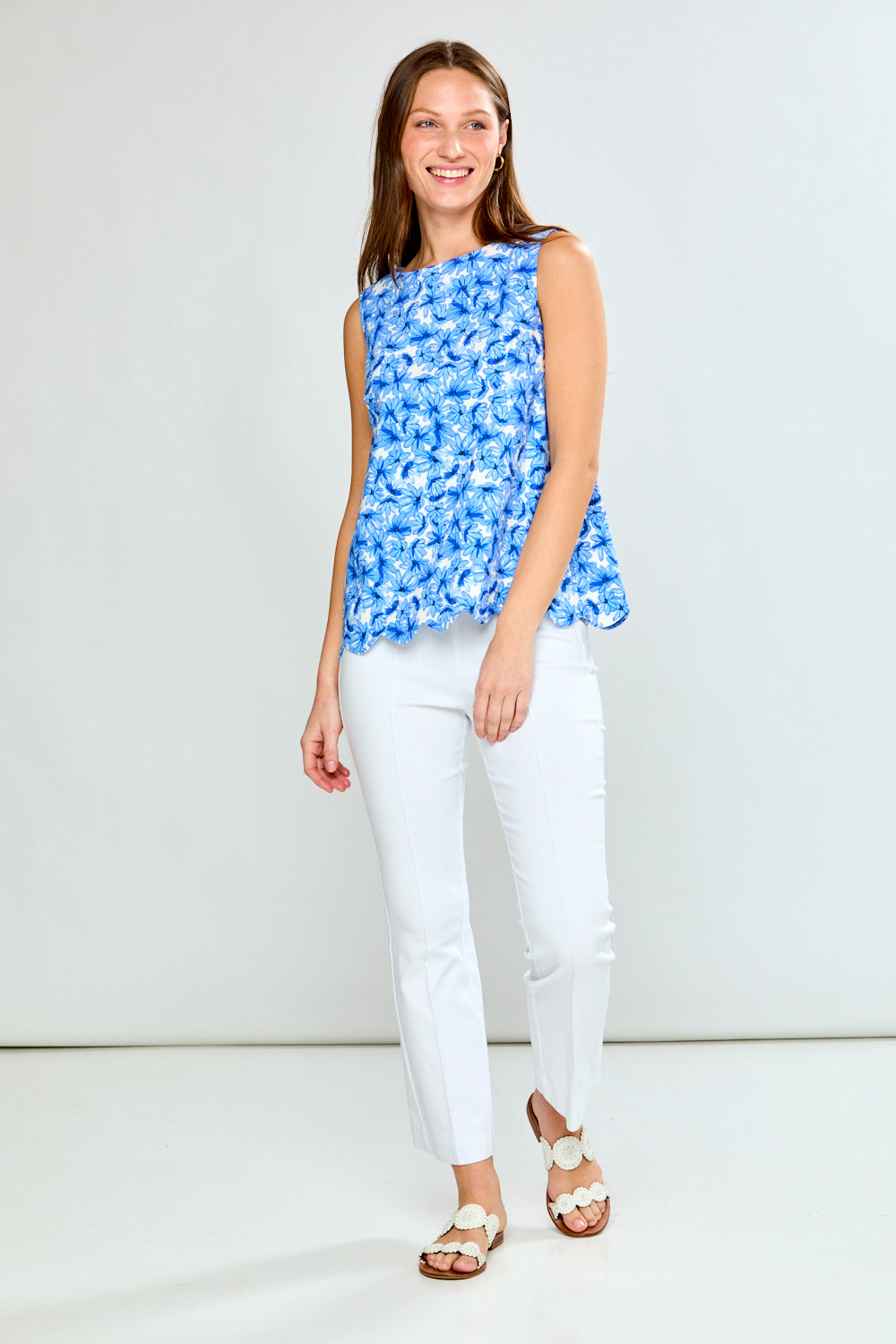 Woman wearing a blue floral top and white pants against a white background