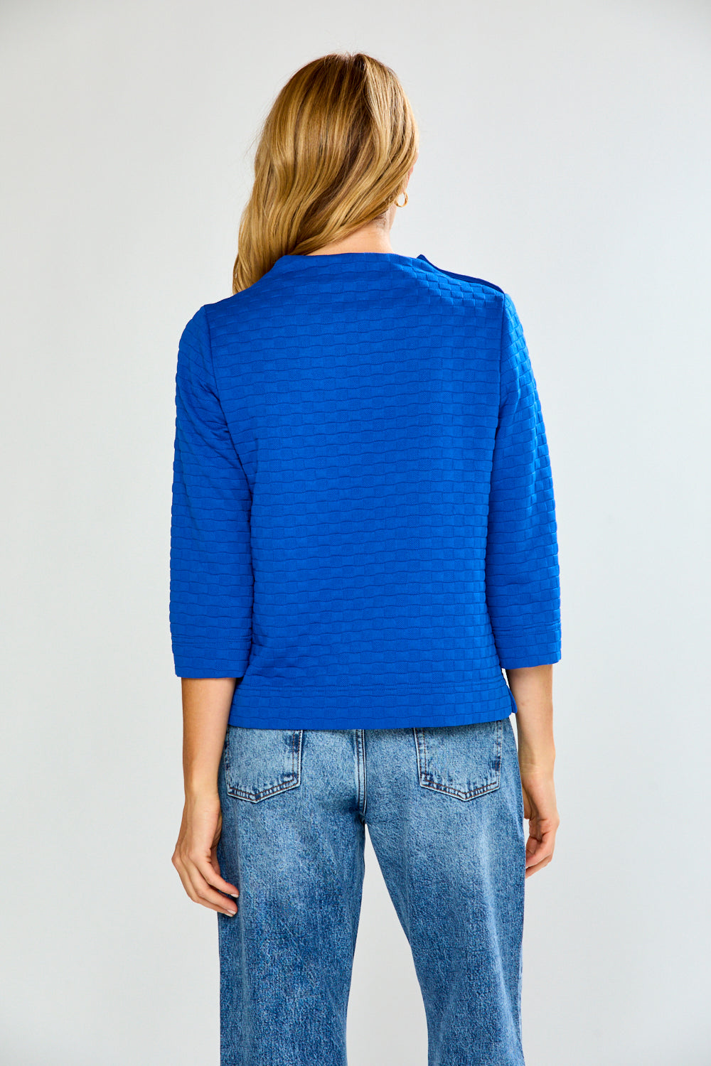 Person wearing a blue textured sweater and jeans on a plain background