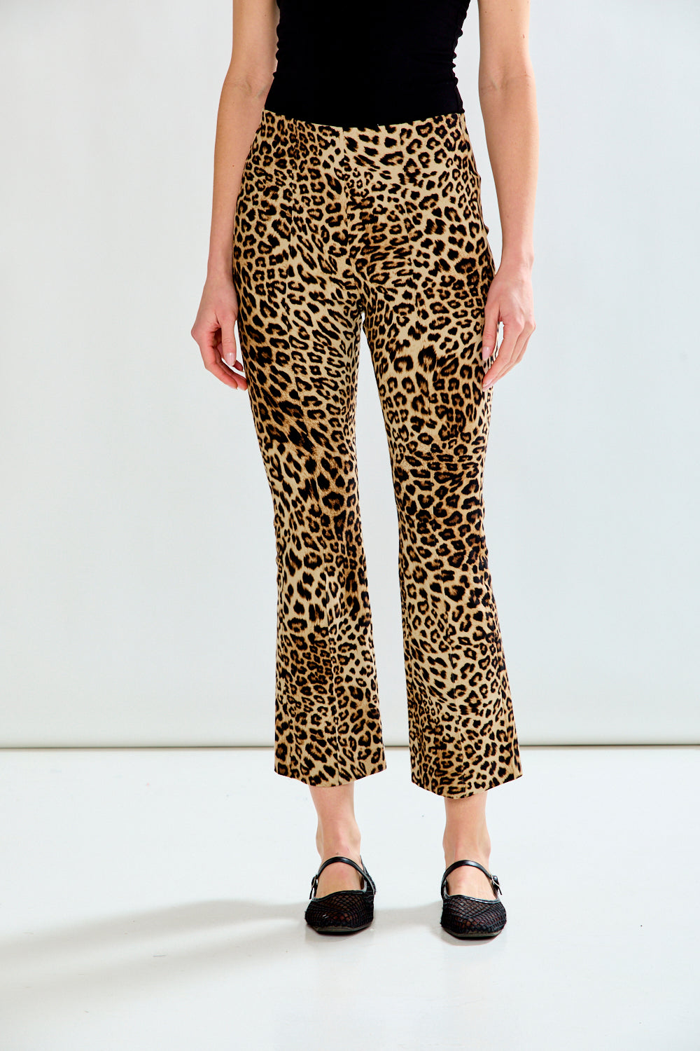 A model wearing leopard-print cropped flare pants with a black top and black flats, shown from the waist down against a plain white studio background.