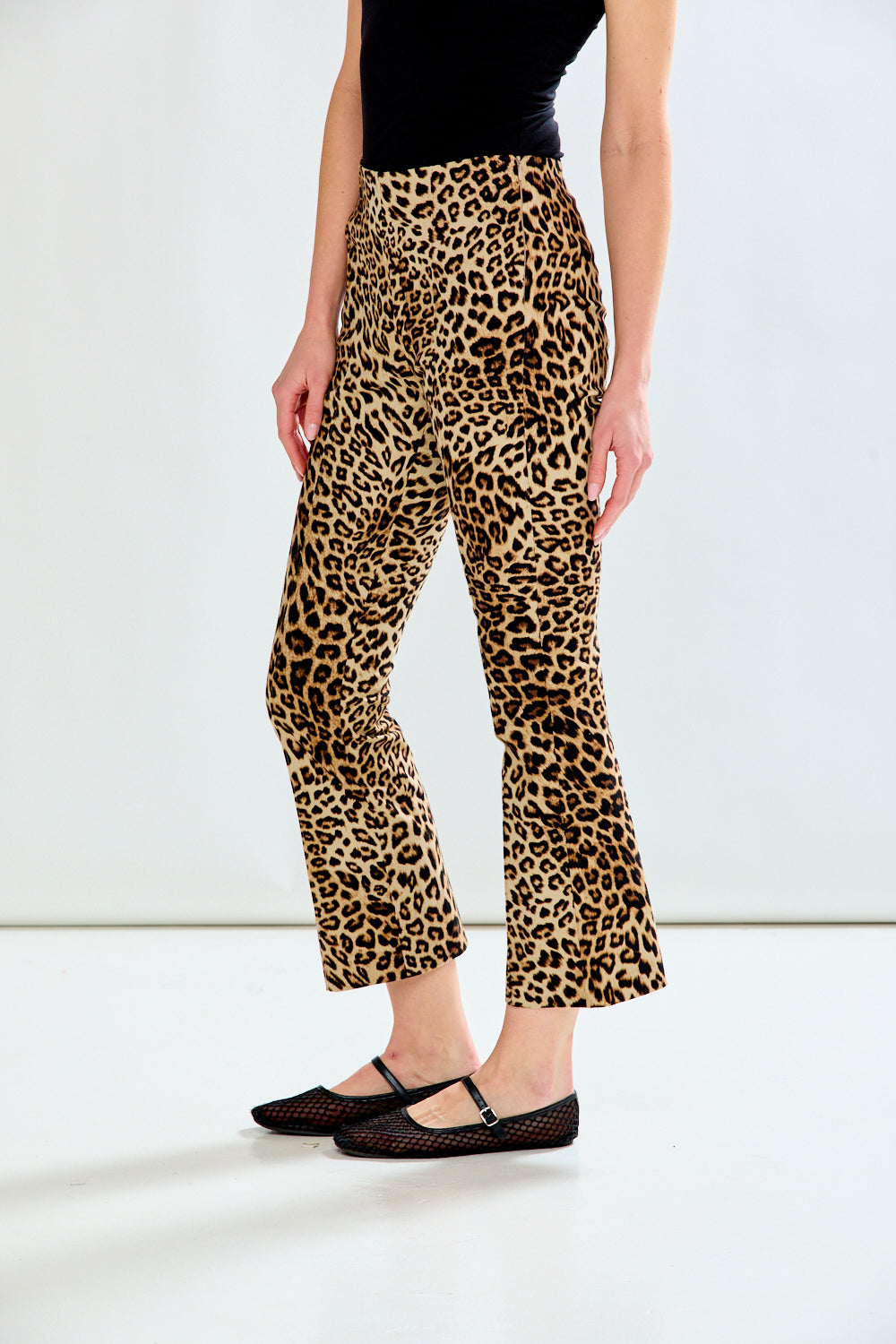 A model wearing leopard-print cropped flare pants with a black top and black flats, shown from the waist down against a plain white studio background.