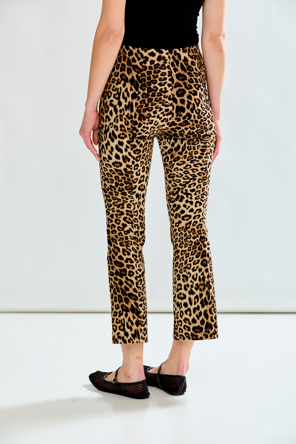 A model from the back wearing leopard print cropped pants, a black top, and black flats, standing against a plain white studio background.