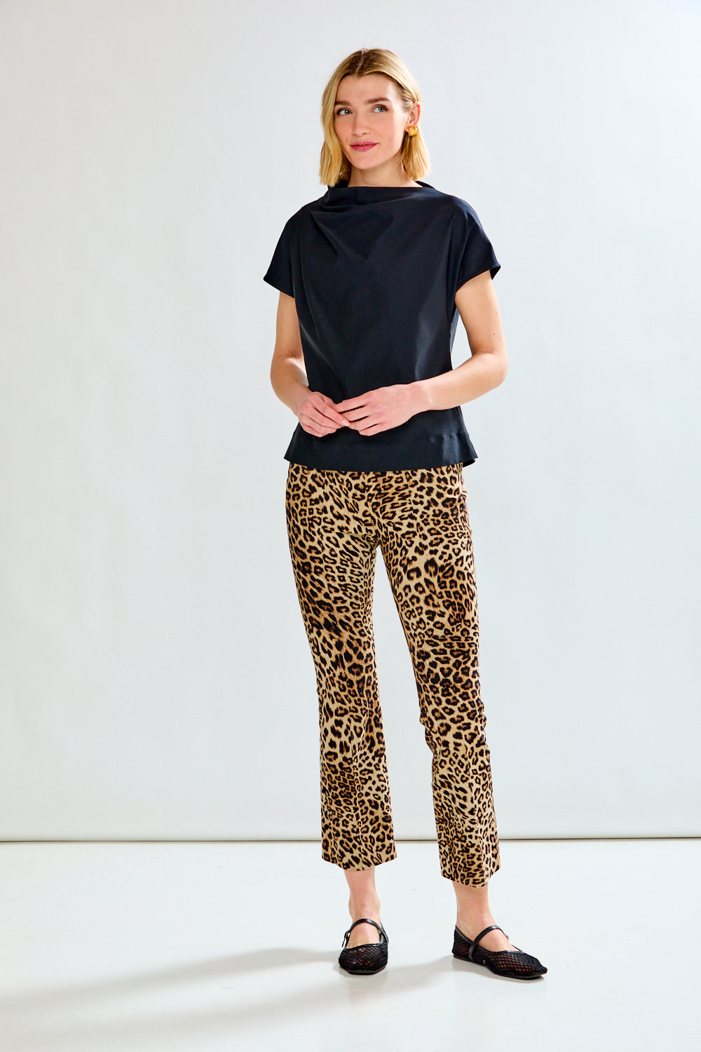 A model wearing leopard-print cropped flare pants with a black top and black flats, shown from the waist down against a plain white studio background.