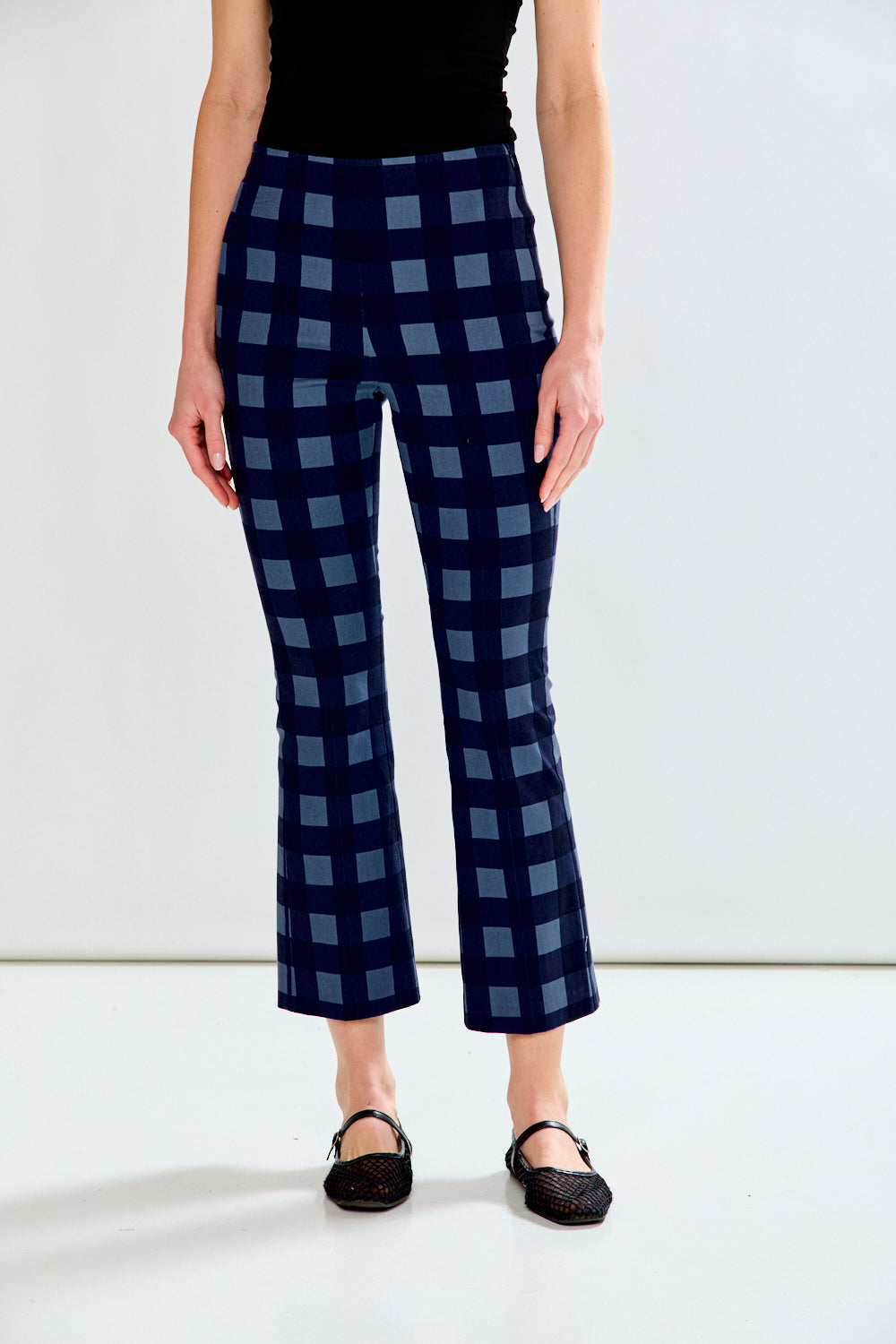 A model is shown from the waist down wearing navy blue cropped pants with a blue checkered pattern, paired with a black top and black flats.