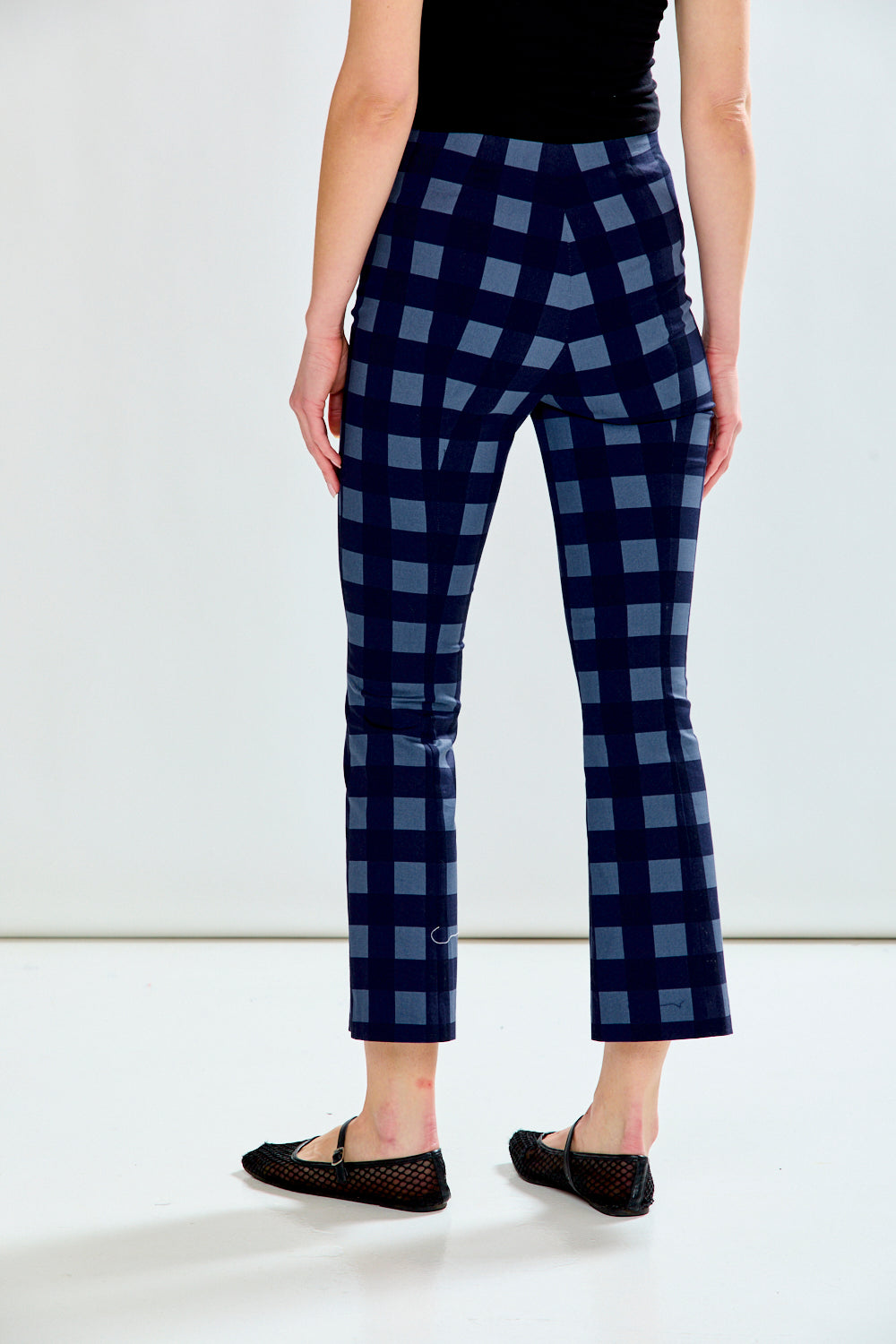 A model is shown from the back wearing navy blue cropped pants with a light blue grid pattern, paired with a black top and black flat shoes.