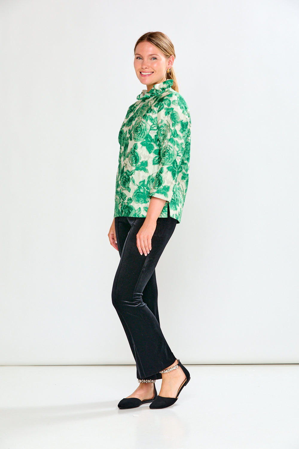Woman wearing a green floral blouse and black pants on a white background