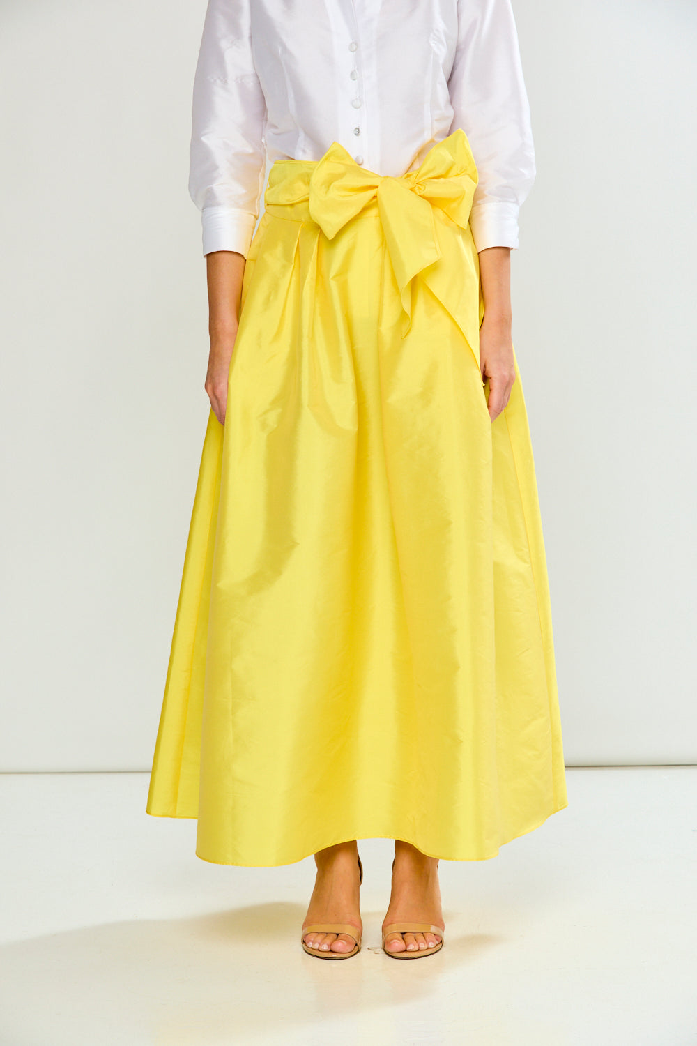 Person wearing a bright yellow skirt with a large bow at the waist on a white background