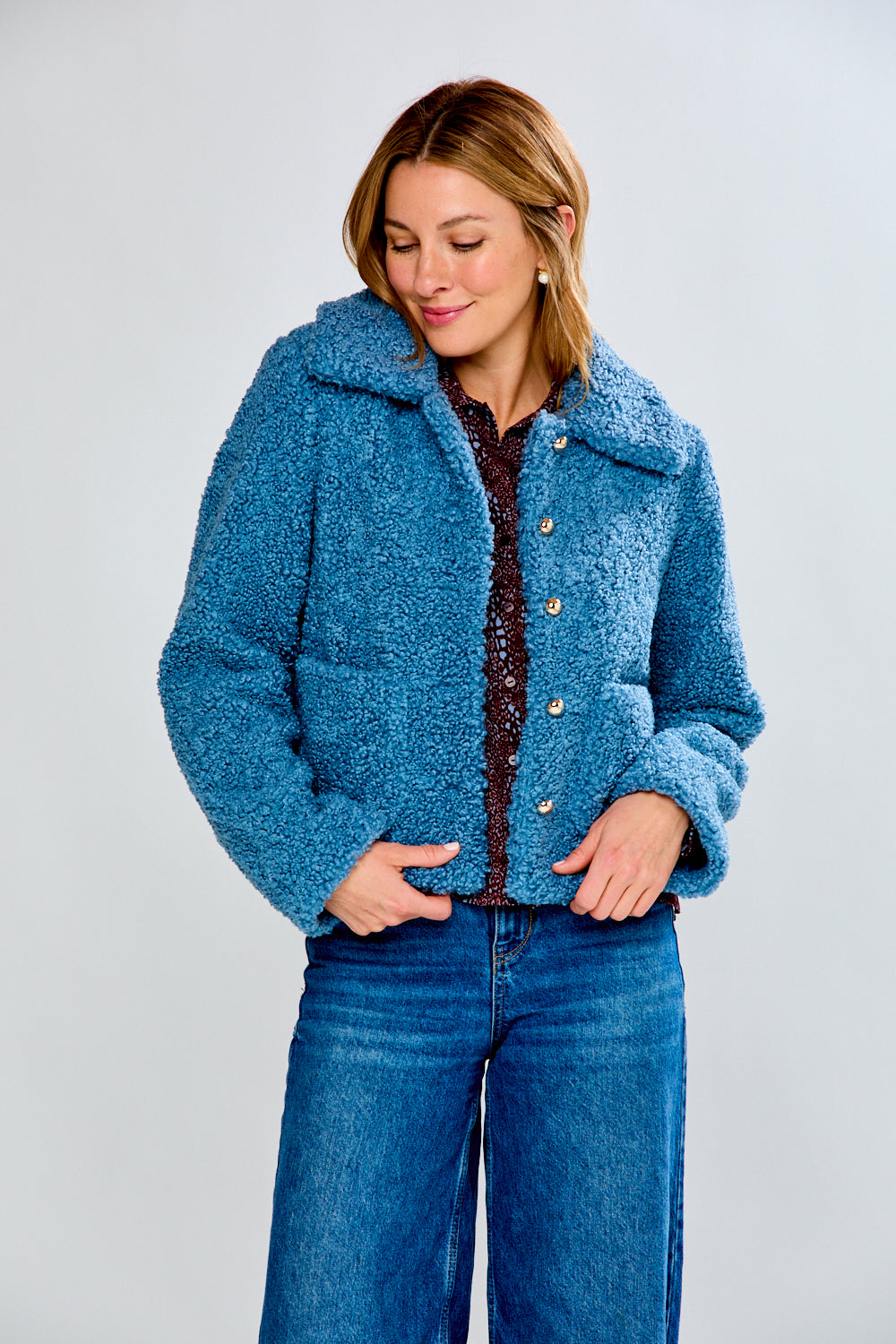 Woman wearing a blue textured jacket and jeans on a plain background