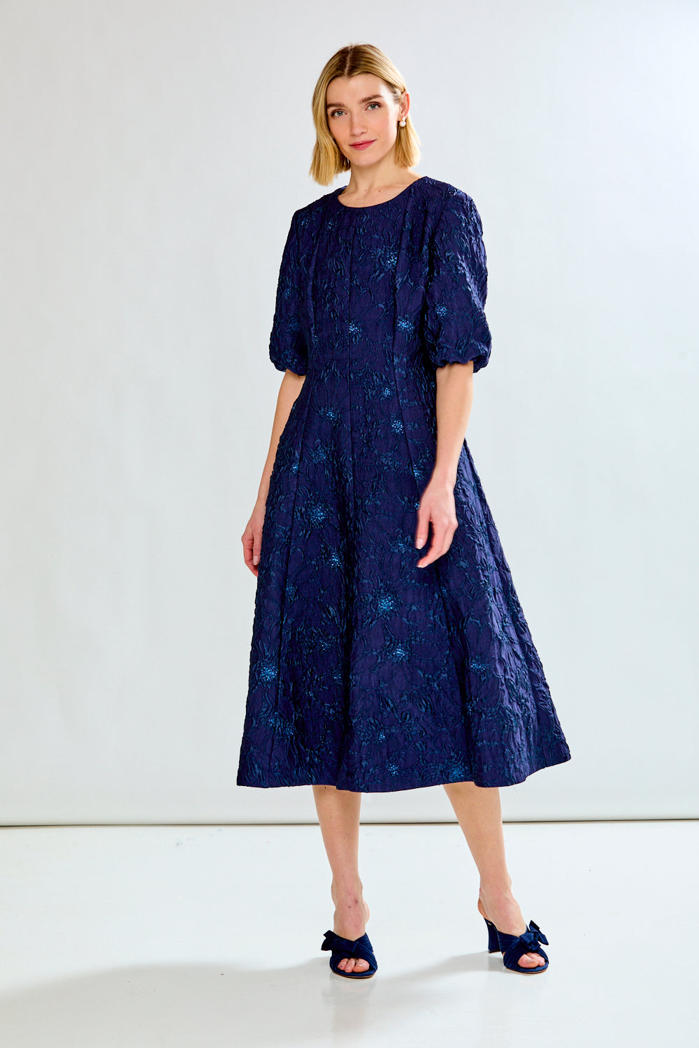 Woman wearing a navy blue dress with a subtle pattern on a white background