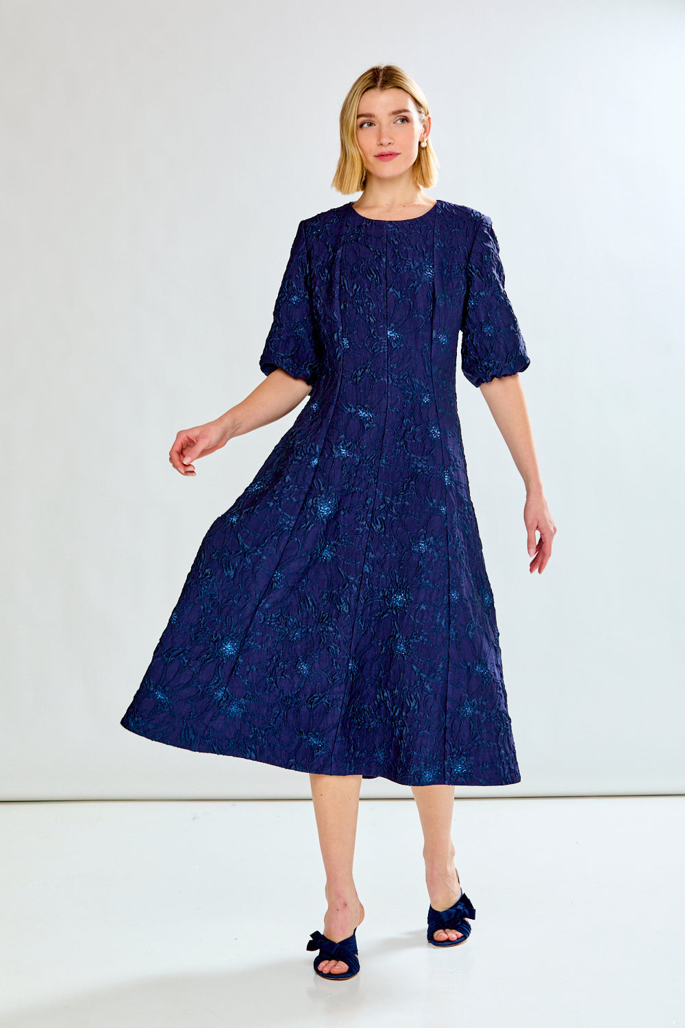 Woman wearing a navy blue dress with a subtle pattern on a white background