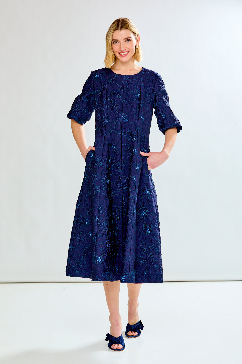 Woman wearing a navy blue dress with a subtle pattern on a white background