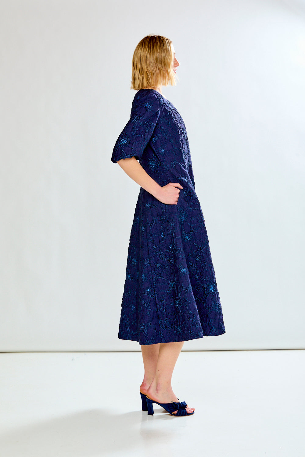 Woman wearing a navy blue dress with a subtle pattern on a white background