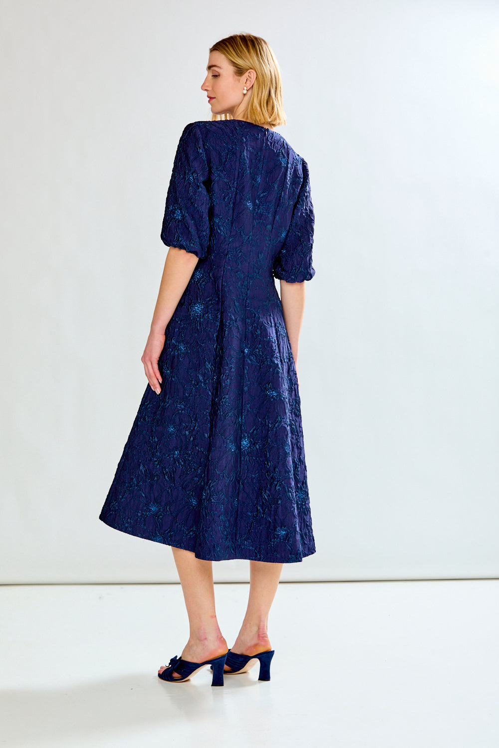Woman wearing a navy blue dress with a subtle pattern on a white background