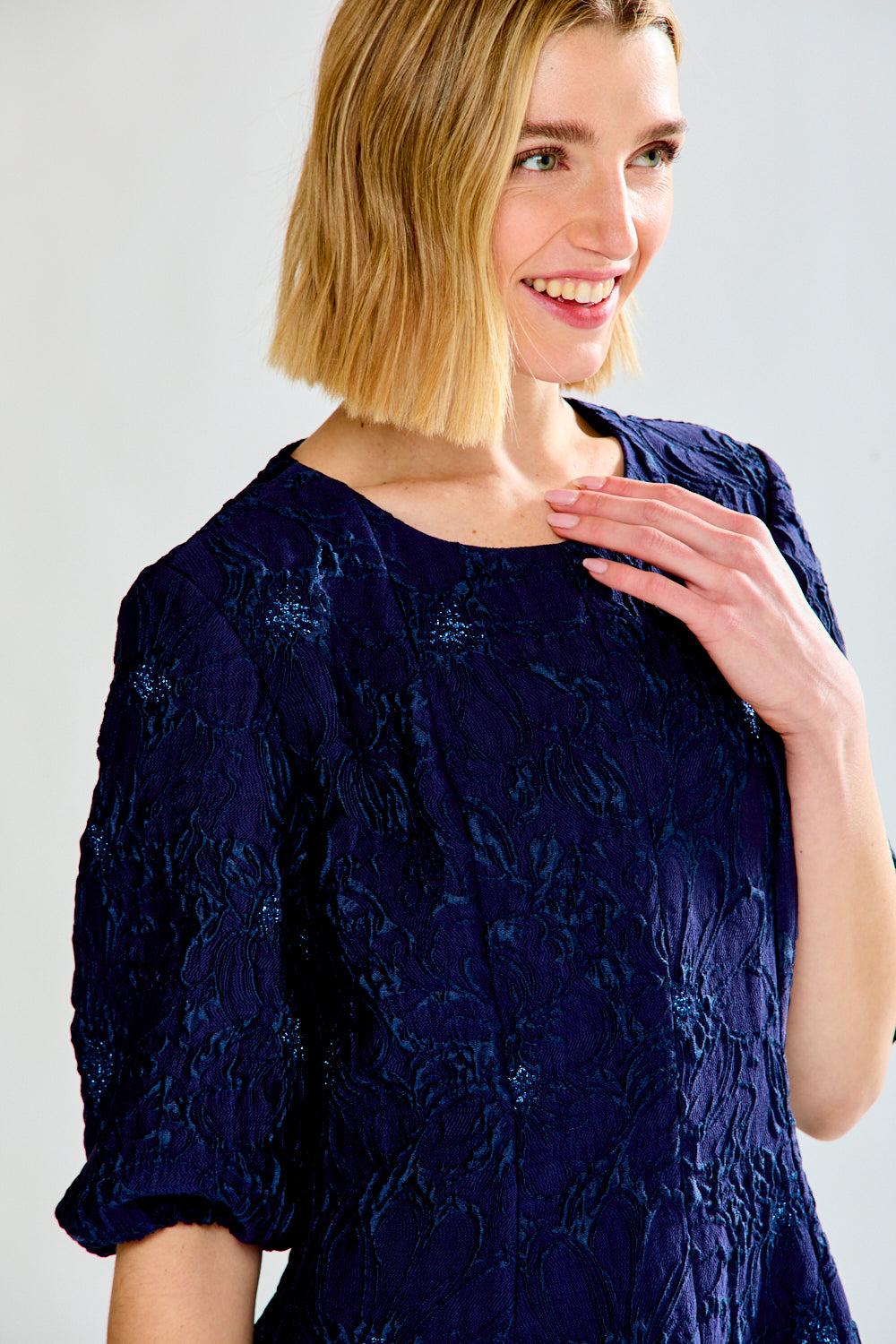 Woman wearing a navy blue dress with a subtle pattern on a white background