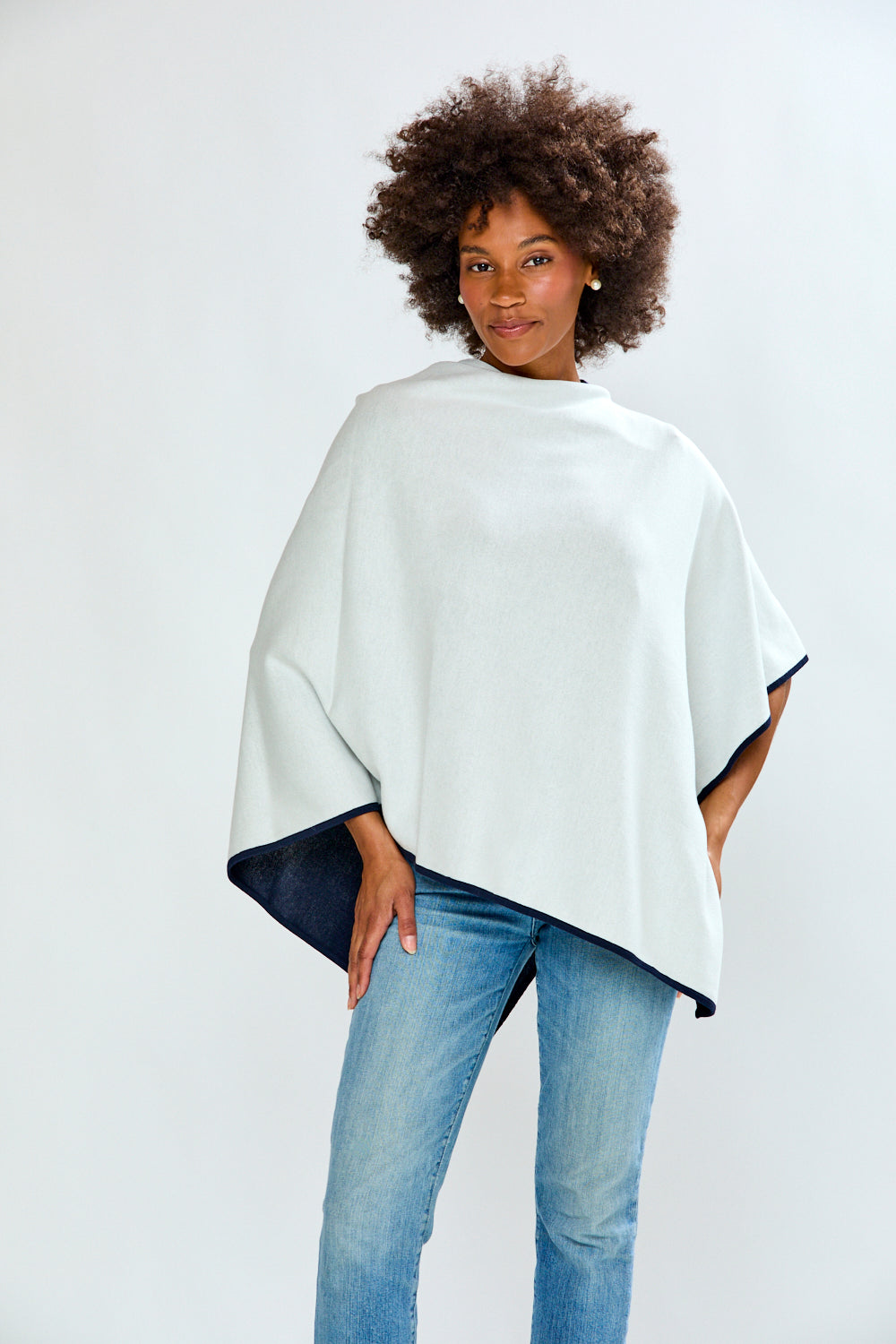 Woman wearing a white poncho with navy accents on a plain background