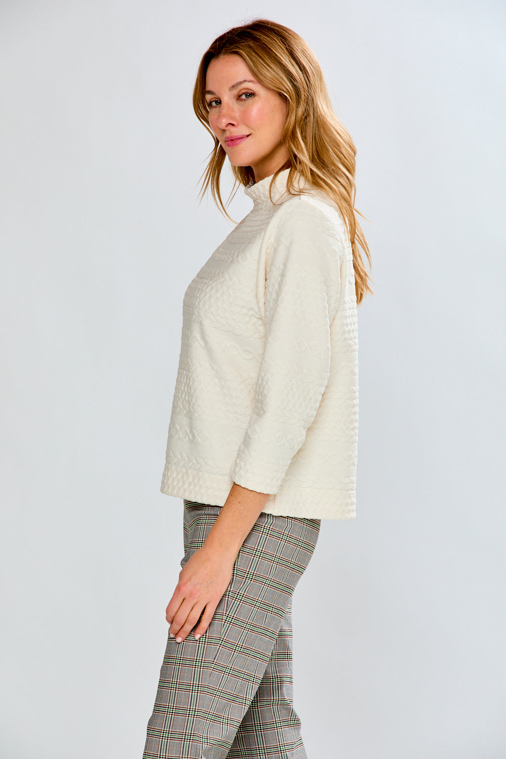Woman wearing a cream sweater and plaid pants against a white background